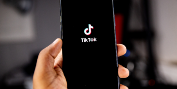hand holding mobile phone with TikTok logo and writing displayed.
